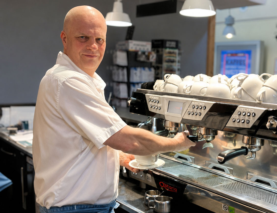 Michael W., Schichtleiter bei Reisdorf, bereitet an einer Kaffeemaschine ein Getränk zu und gibt Einblick in seinen Arbeitsalltag am Rasthof Dresdner Tor Nord.